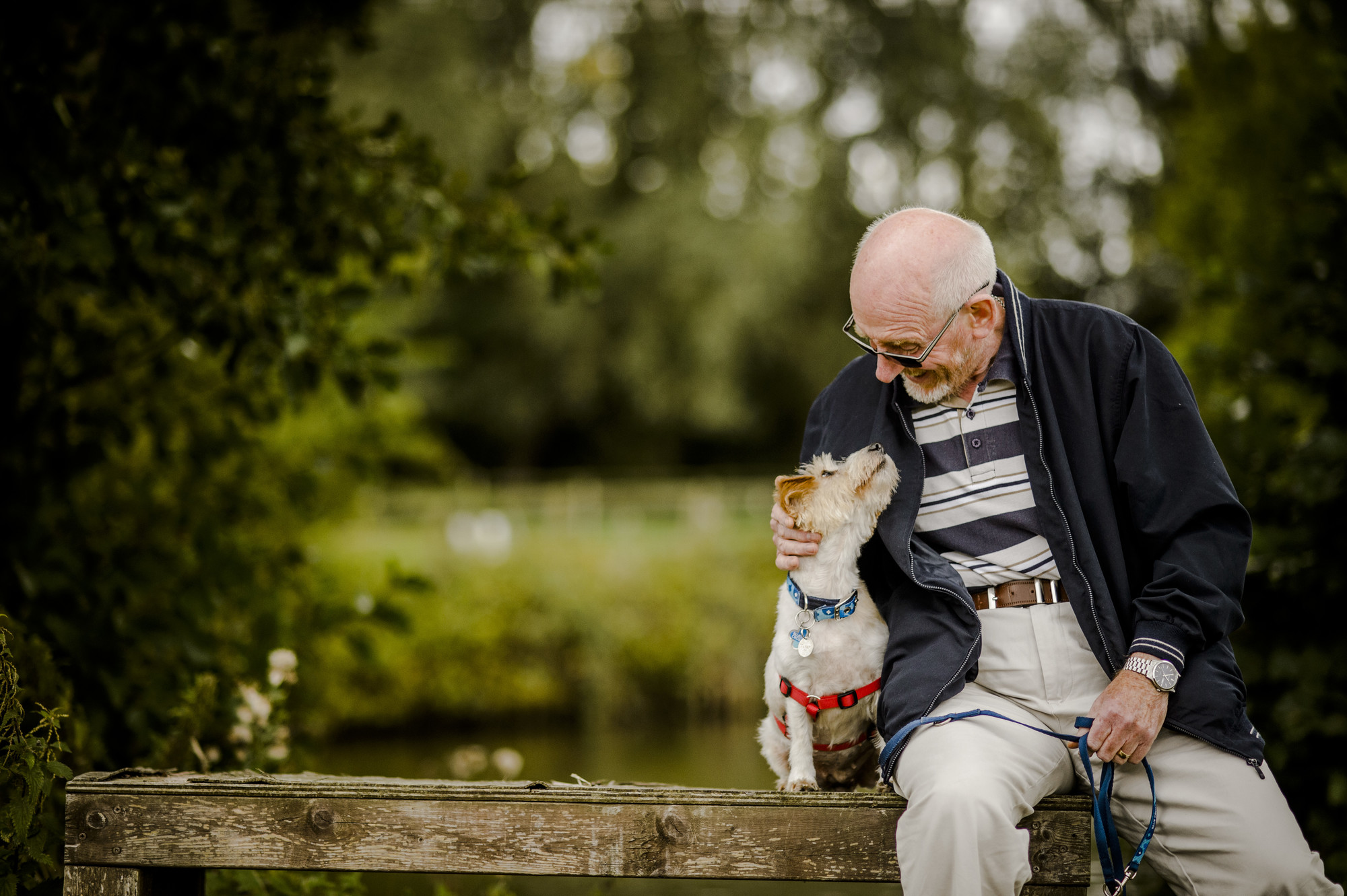 Photo of a jack russell terrier sitting next to a man. They are both looking at each other and smiling.