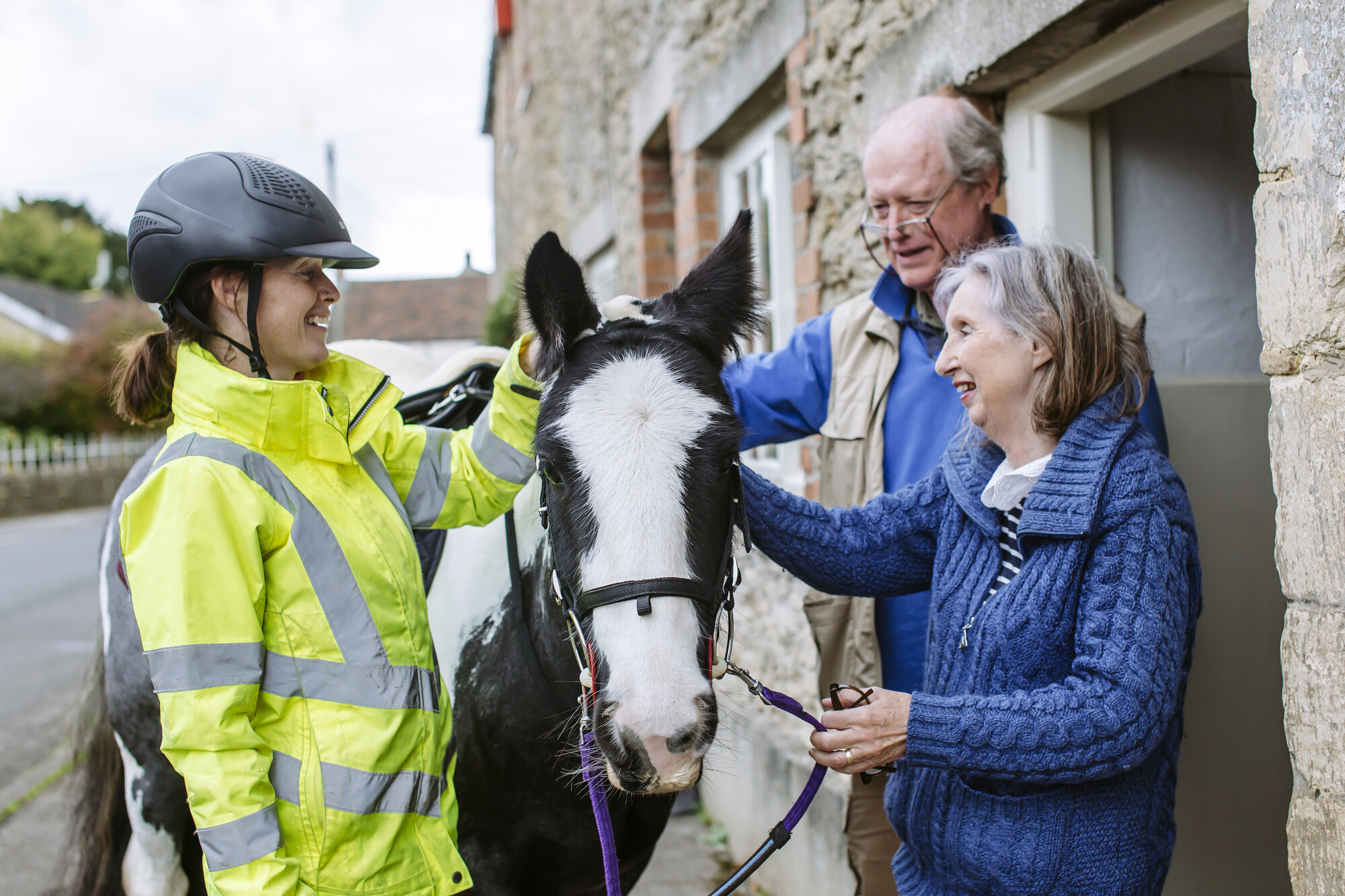 Black and white horse is stroked by woman and man outside their home