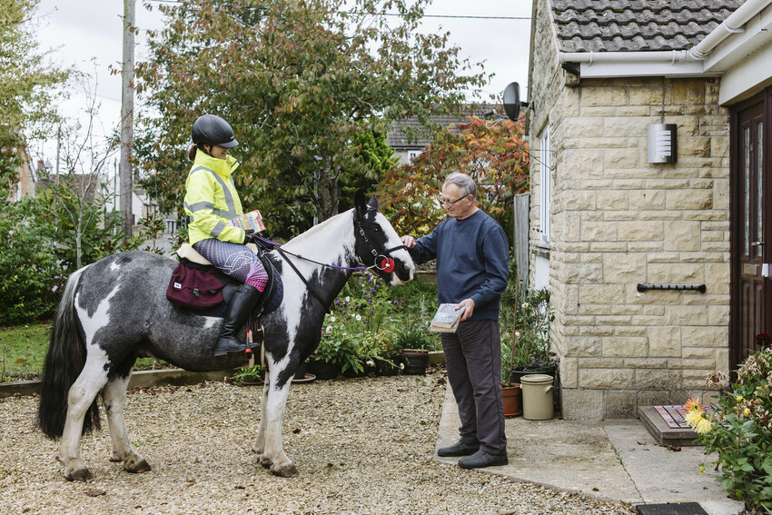 Abi on horseback passing over a book to member of the village