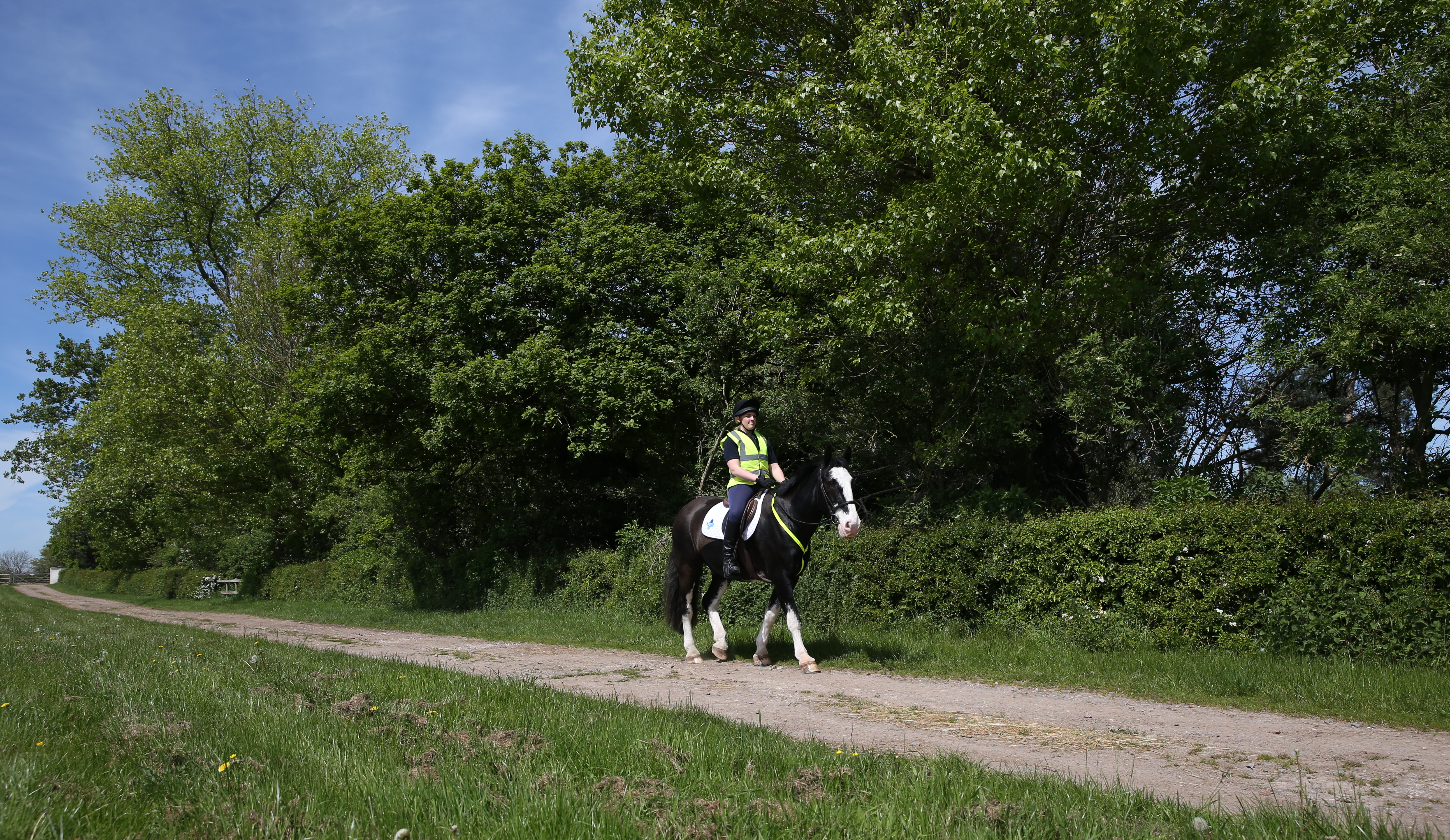 Image shows a female rider wearing a high vis jacket riding a black and white horse along a track