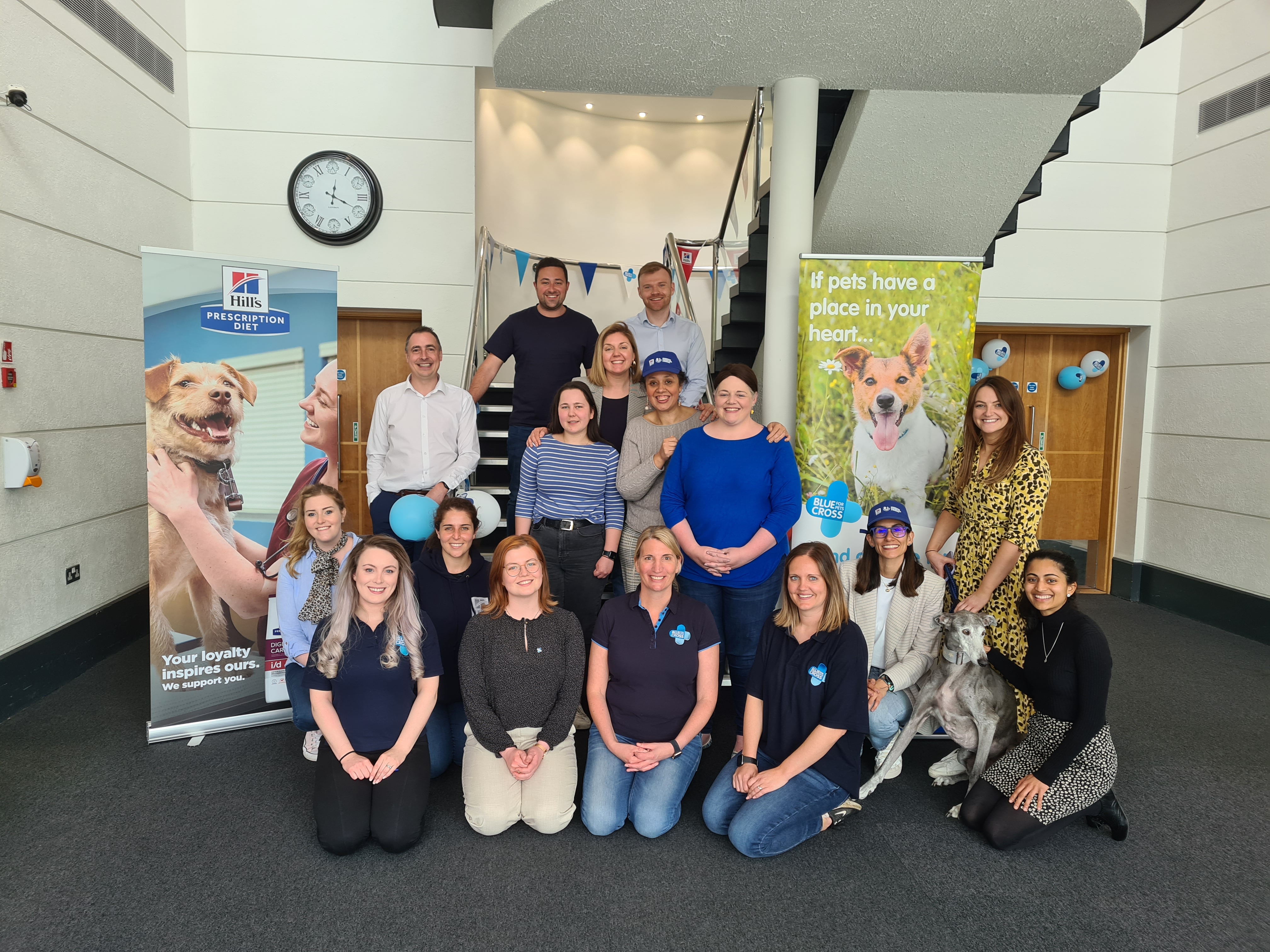 Blue Cross partner with Hills pet food. Blue Cross and Hills staff pose in front of Hills and Blue Cross banners.