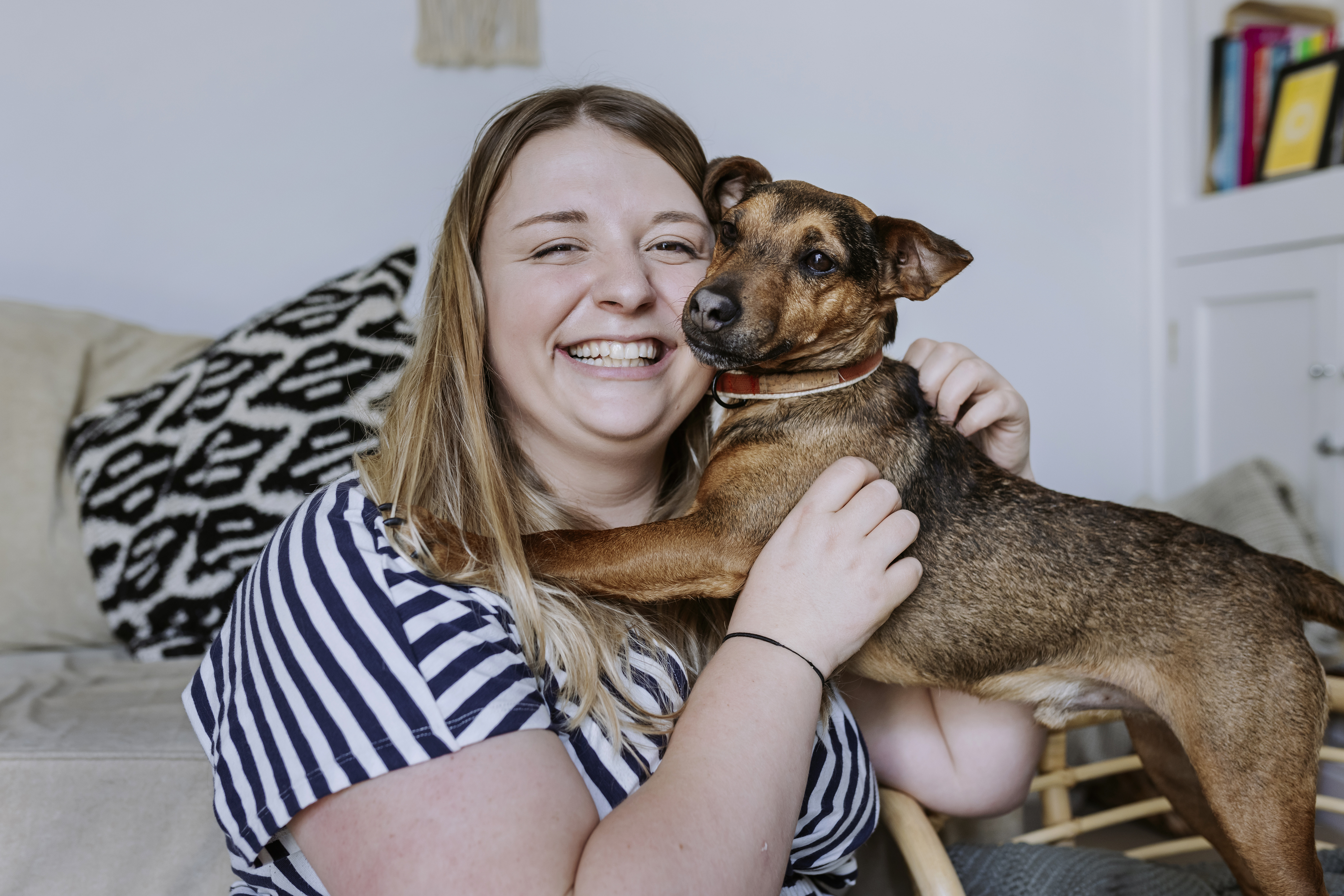 Albert cuddles up to his owner Johannah on the sofa. They both smile towards the camera.