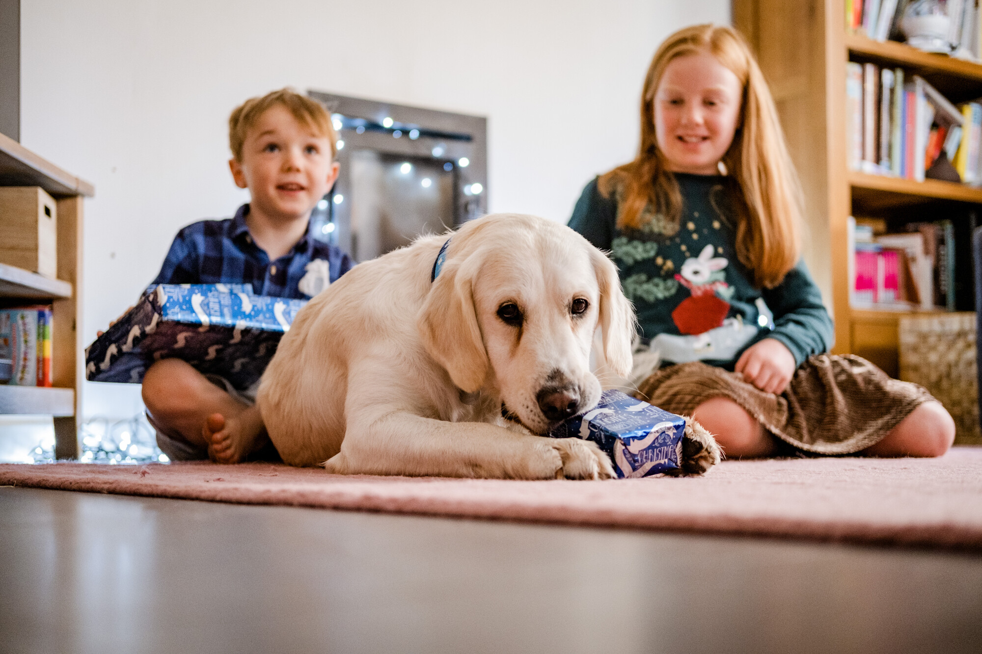 Amber opening a Christmas present with Laurence and Sophie excitedly looking on in background