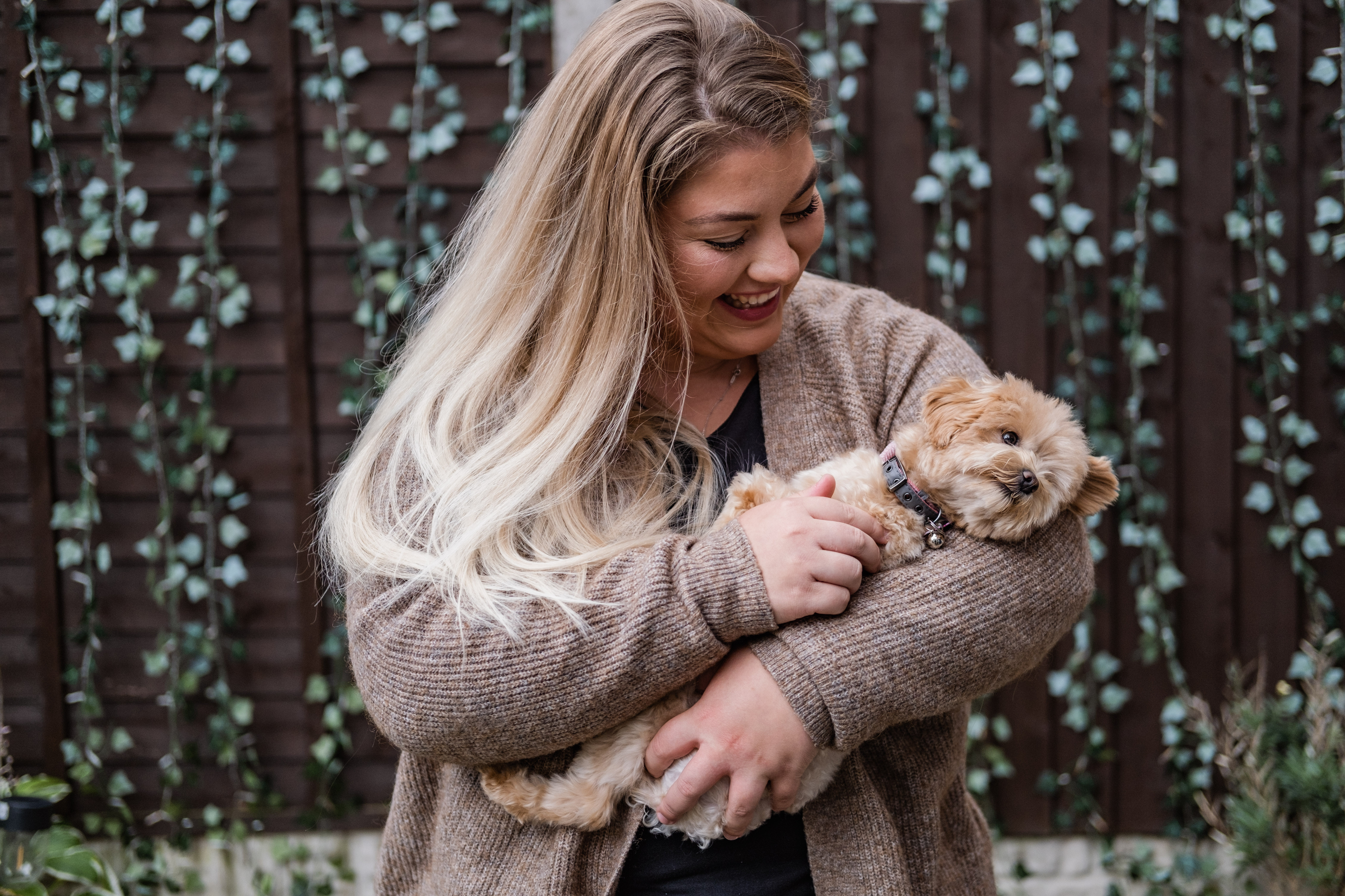A golden toy poodle is cuddled in the arms of her smiling owner