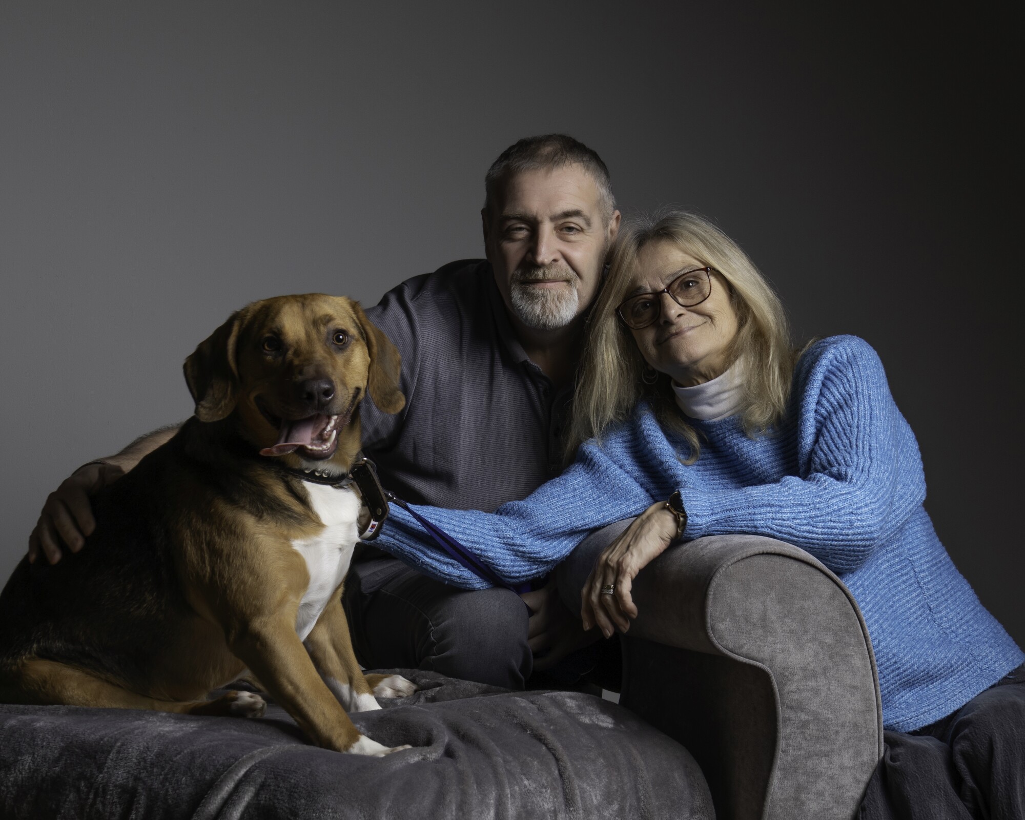 Dog Bagel with his new owners sitting on a grey sofa