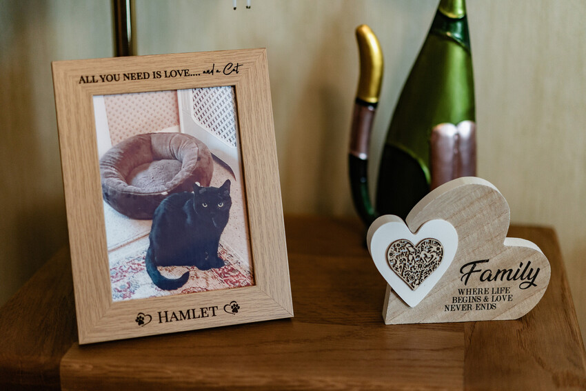 A picture of a black cat in a phote frame, which reads 'All you need is love... and a cat. Hamlet' on a side table