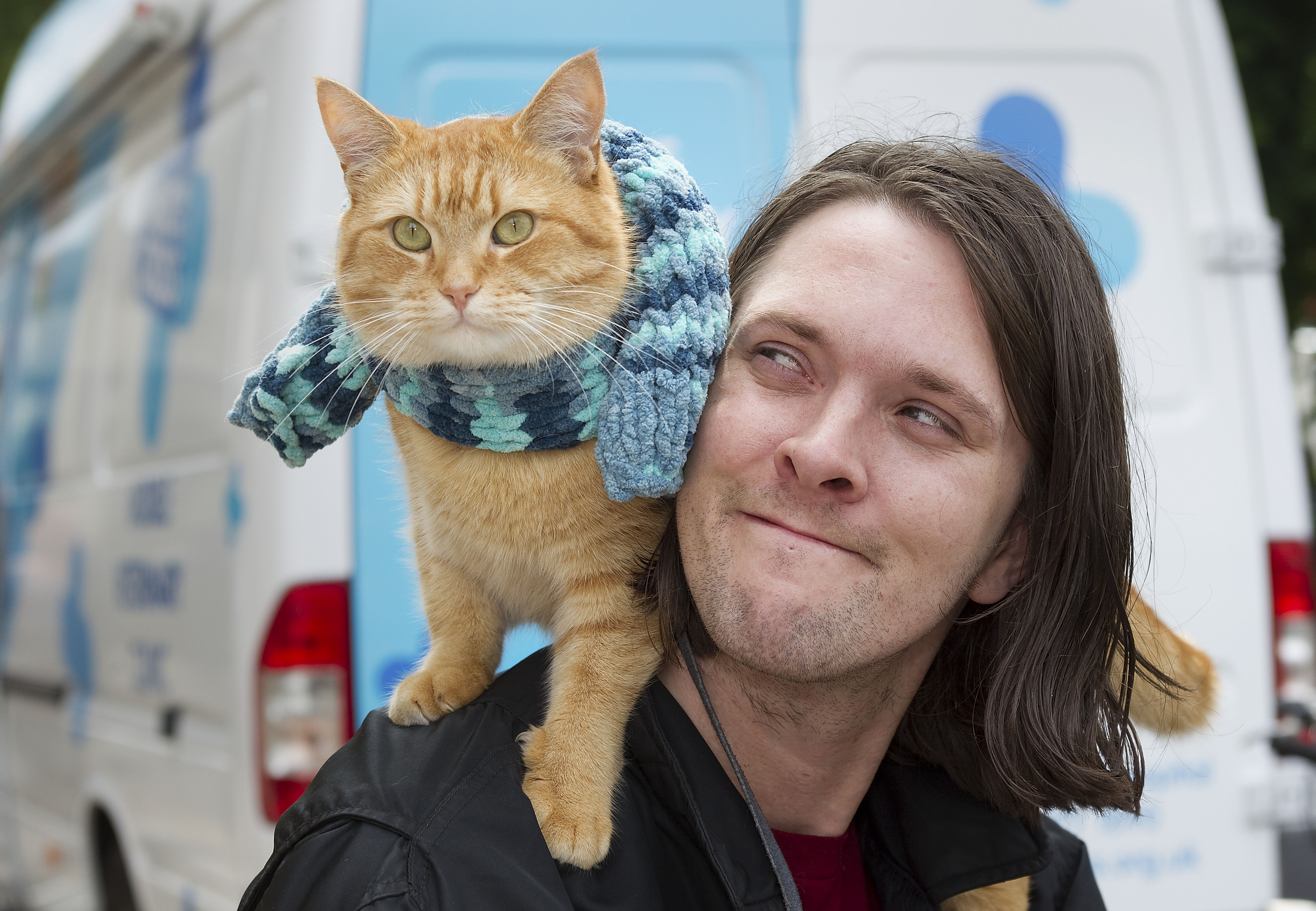 Street cat Bob sits on James Bowen's shoulder by the Blue Cross mobile clinic which helped them through tough times