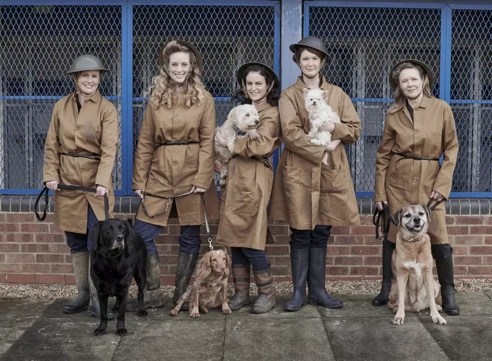 Five women with five dogs, dressed in 1940s overcoats and black boots