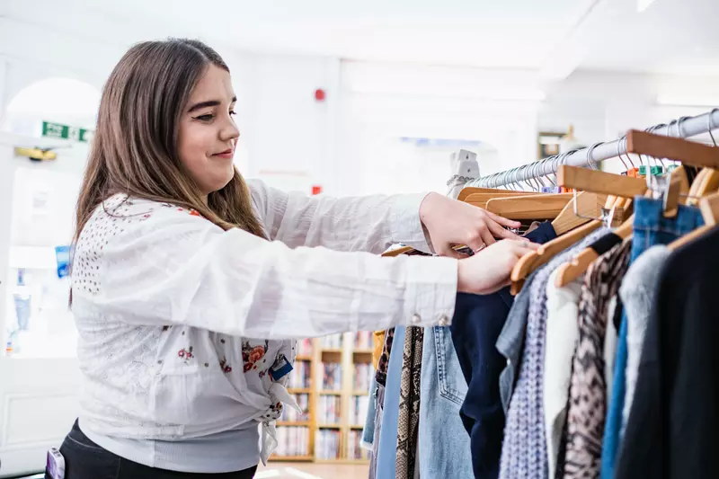 Charity shop volunteer Jess organises a railing of clothing.