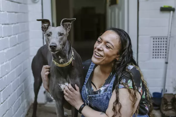 Rescued greyhound Bleu and her owner Amy, sit side by side. Amy embraces Bleu, who looks at the camera.