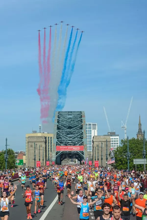 Runners participating in the AJ Bell Great North Run. In the background, the Red Arrows fly overhead, creating streams of colourful smoke.