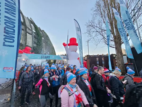 A group of participants at the start of the London Winter Walk route. They are dressed in bobble hats and scarves. There is a big snow man in the background.