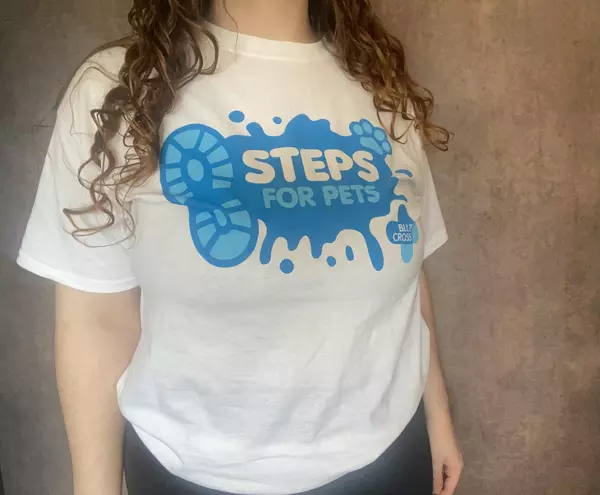A lady modelling a Steps for Pets t-shirt. The t-shirt is white with a large blue Steps for Pets logo printed across the front