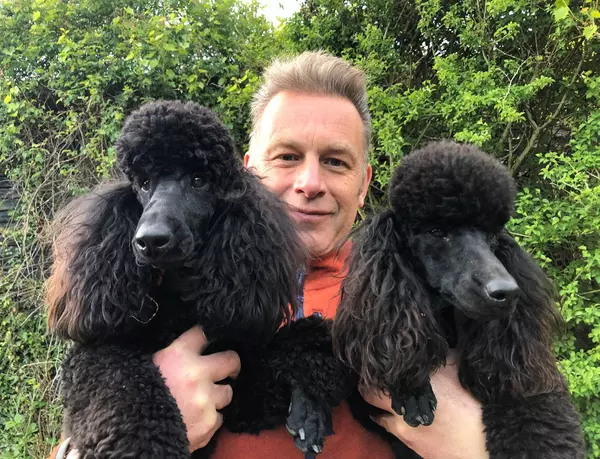 Chris Packham, a man with short light hair smiling and holding two black poodles.
