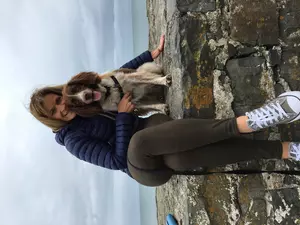 Liver and white springer spaniel Bailey looks happily at the camera as a woman in activewear hugs him