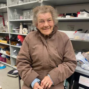 An elderly lady who uses Blue Cross pet food banks, sitting on a chair in the pet food bank warehouse