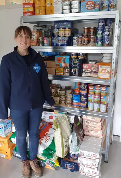 A Blue Cross member of staff standing next to shelves of pet food