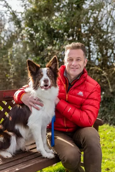 Brown and white border collie sat on a bench next to Chris Packham