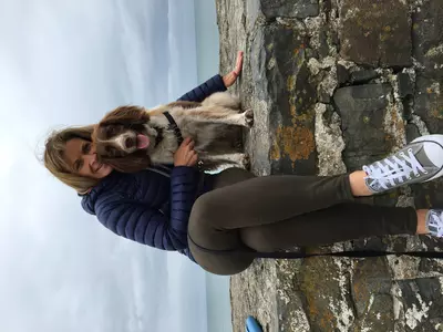 Liver and white springer spaniel Bailey looks happily at the camera as a woman in activewear hugs him