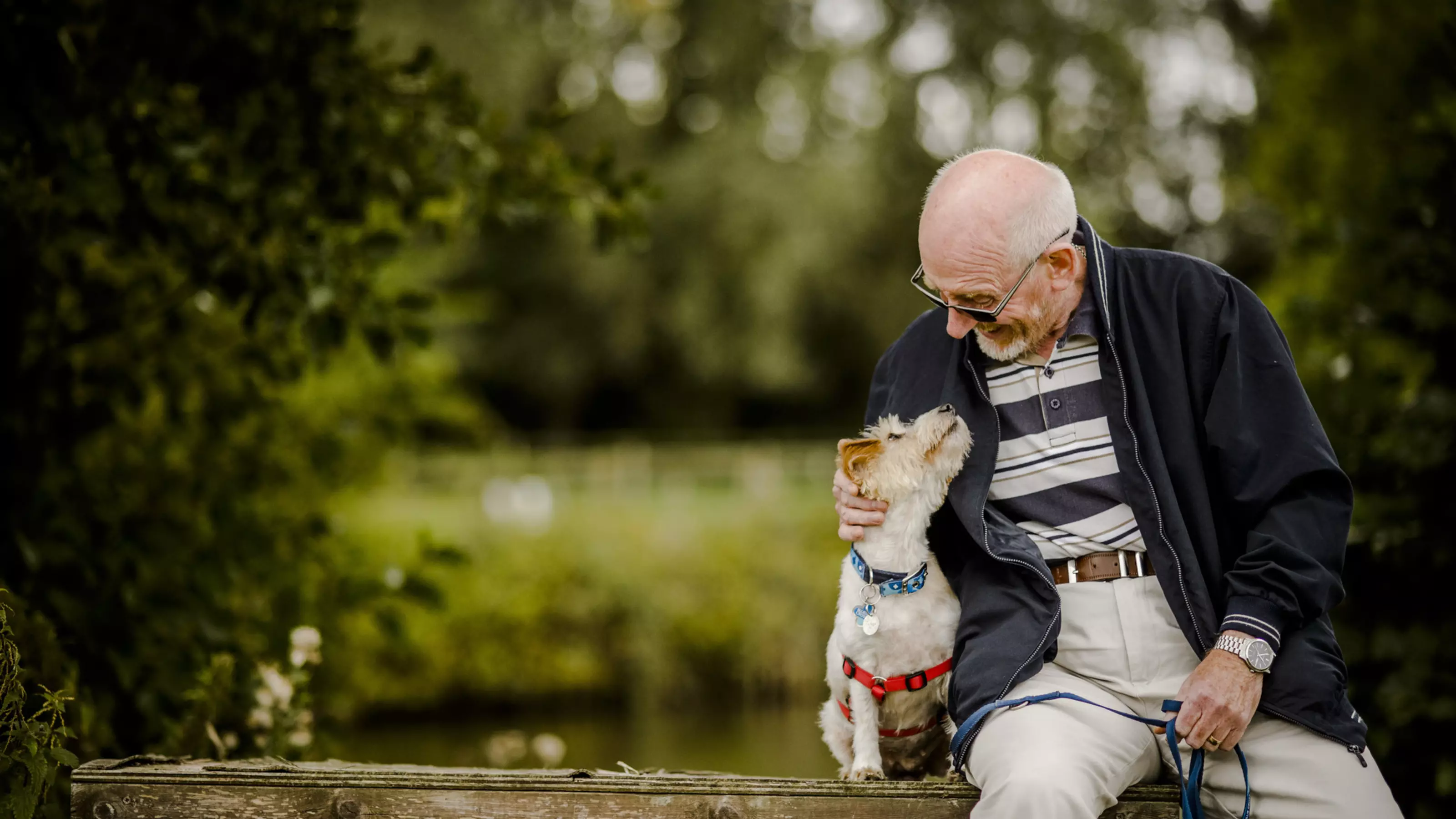 Photo of a jack russell terrier sitting next to a man. They are both looking at each other and smiling.