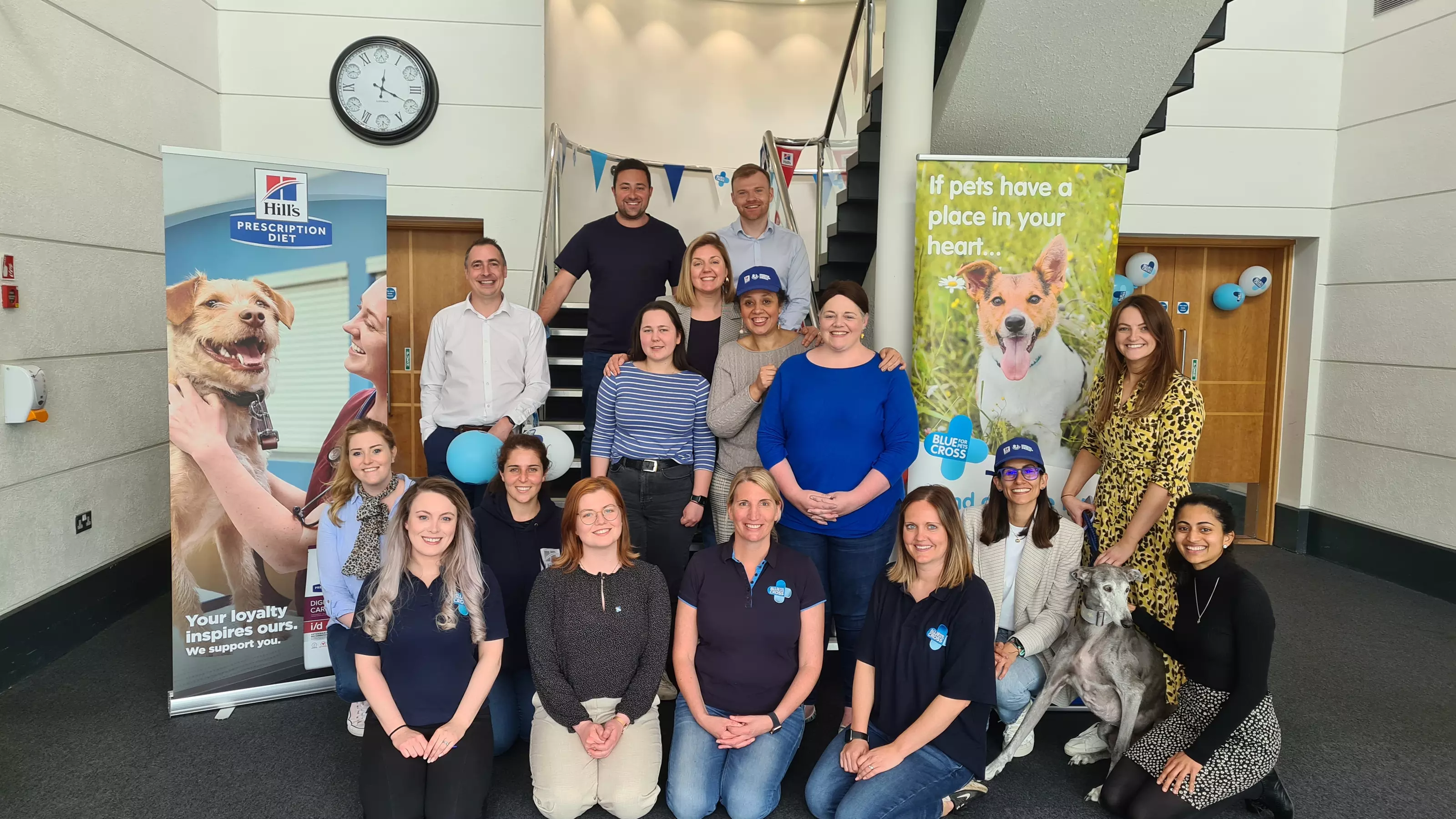 Blue Cross partner with Hills pet food. Blue Cross and Hills staff pose in front of Hills and Blue Cross banners.