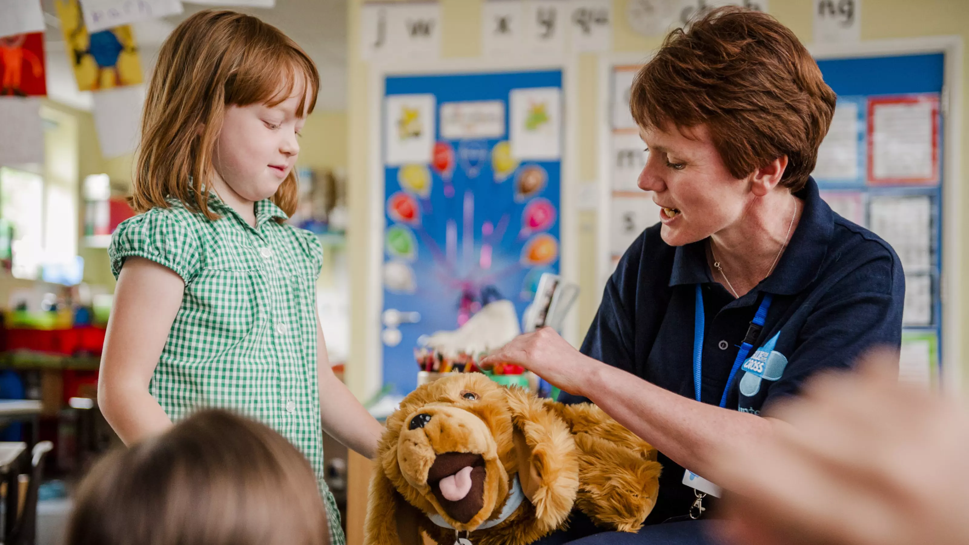 A Blue Cross female volunteer stroking a toy dog and a school girl watching
