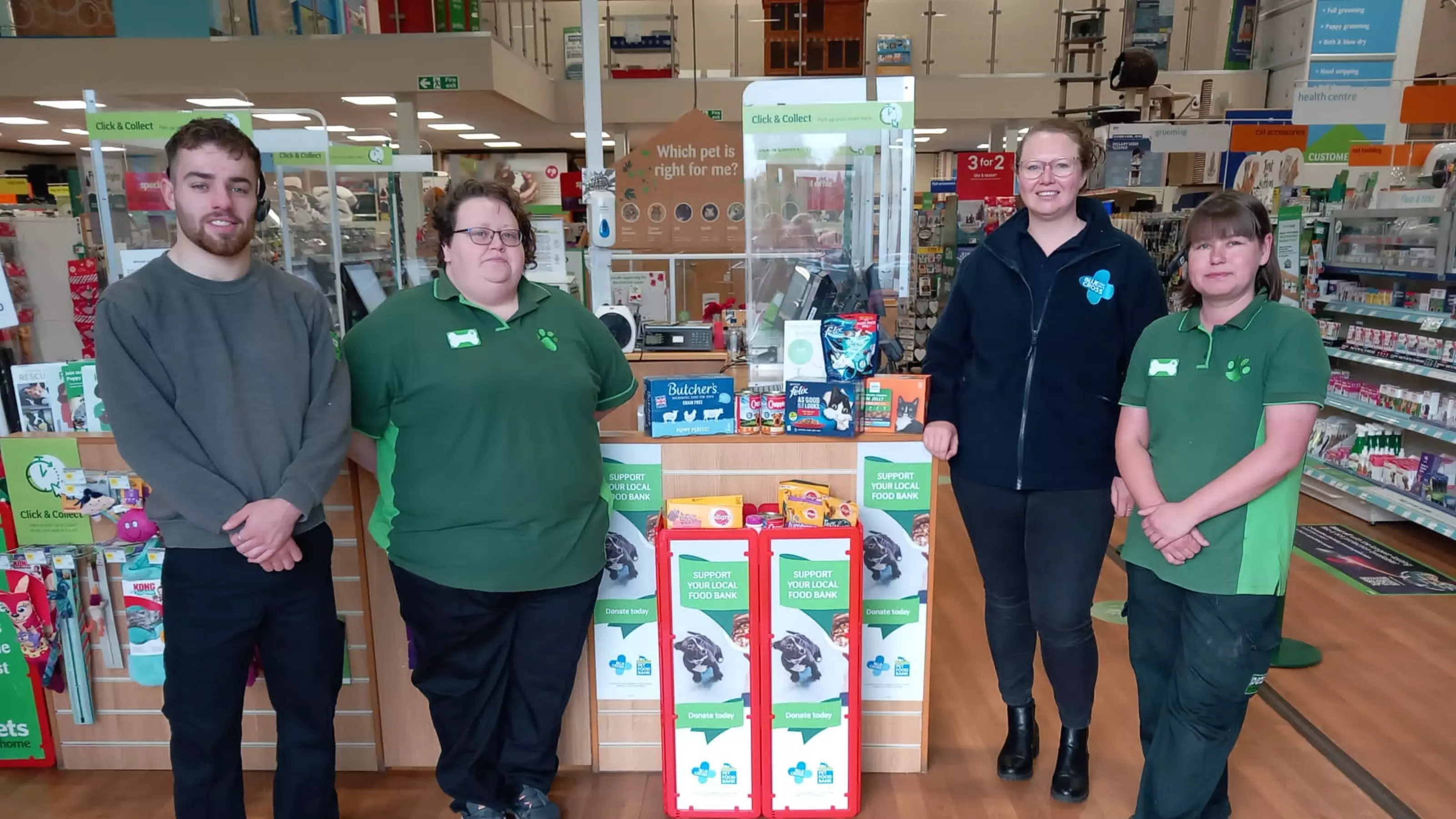 Four members of staff stand in a Pets at Home store with a pet food bank donation point at the till