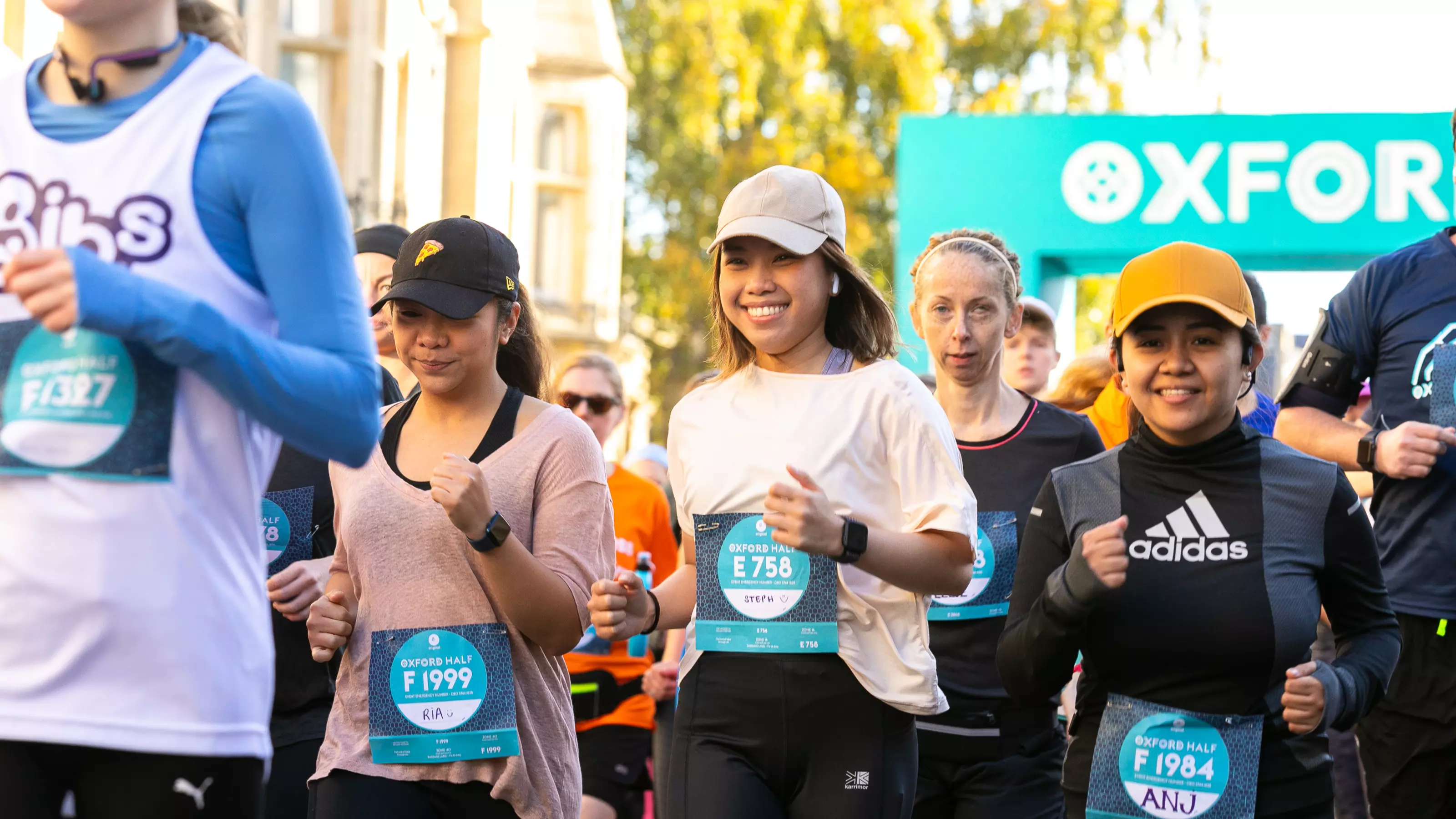 A group of runners taking part in the Oxford Half marathon. They are wearing caps and running gear, and smiling in the sunshine.
