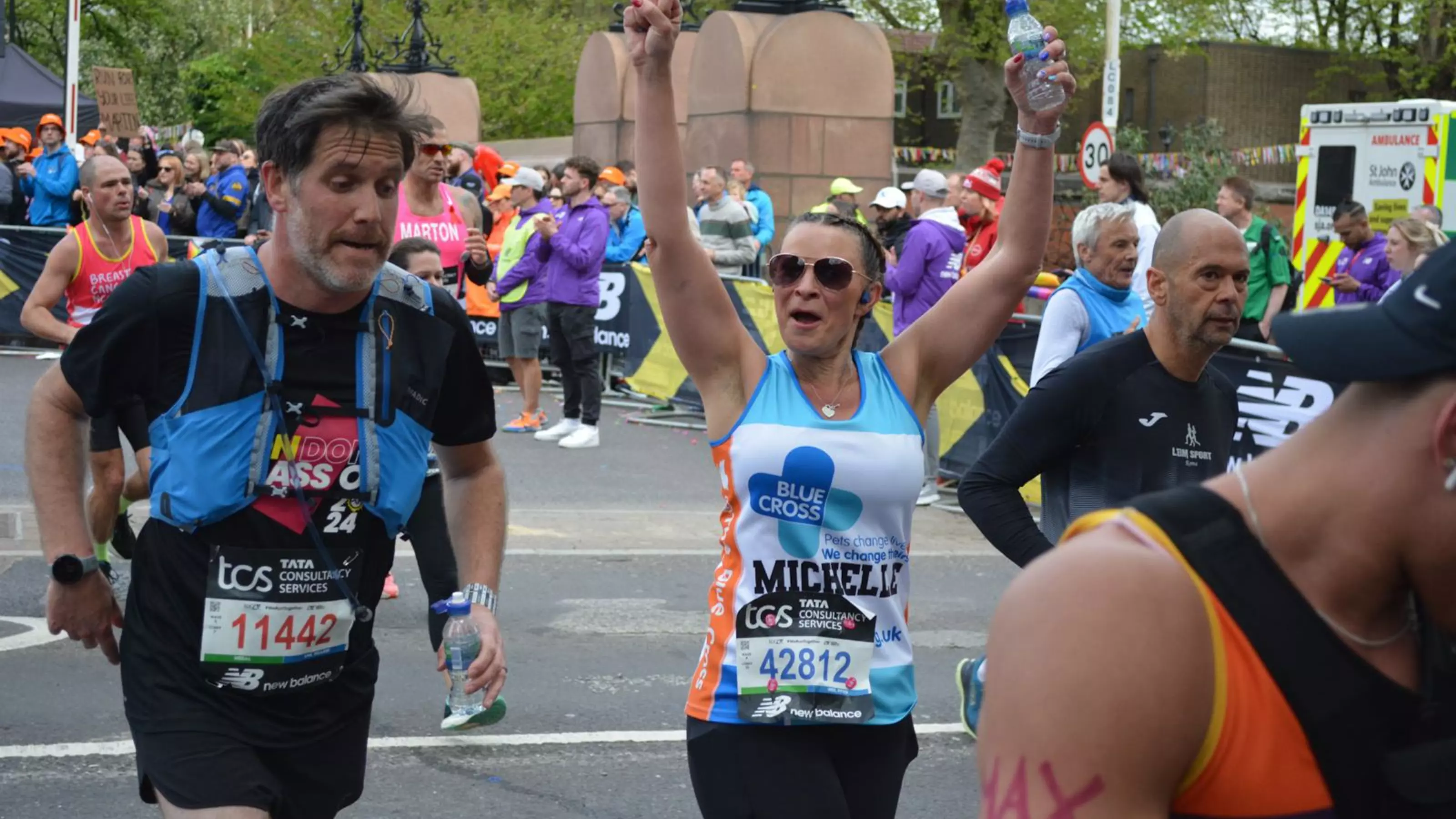 A woman participating in London Marathon, representing Blue Cross. She is holding her arms up in a cheer.