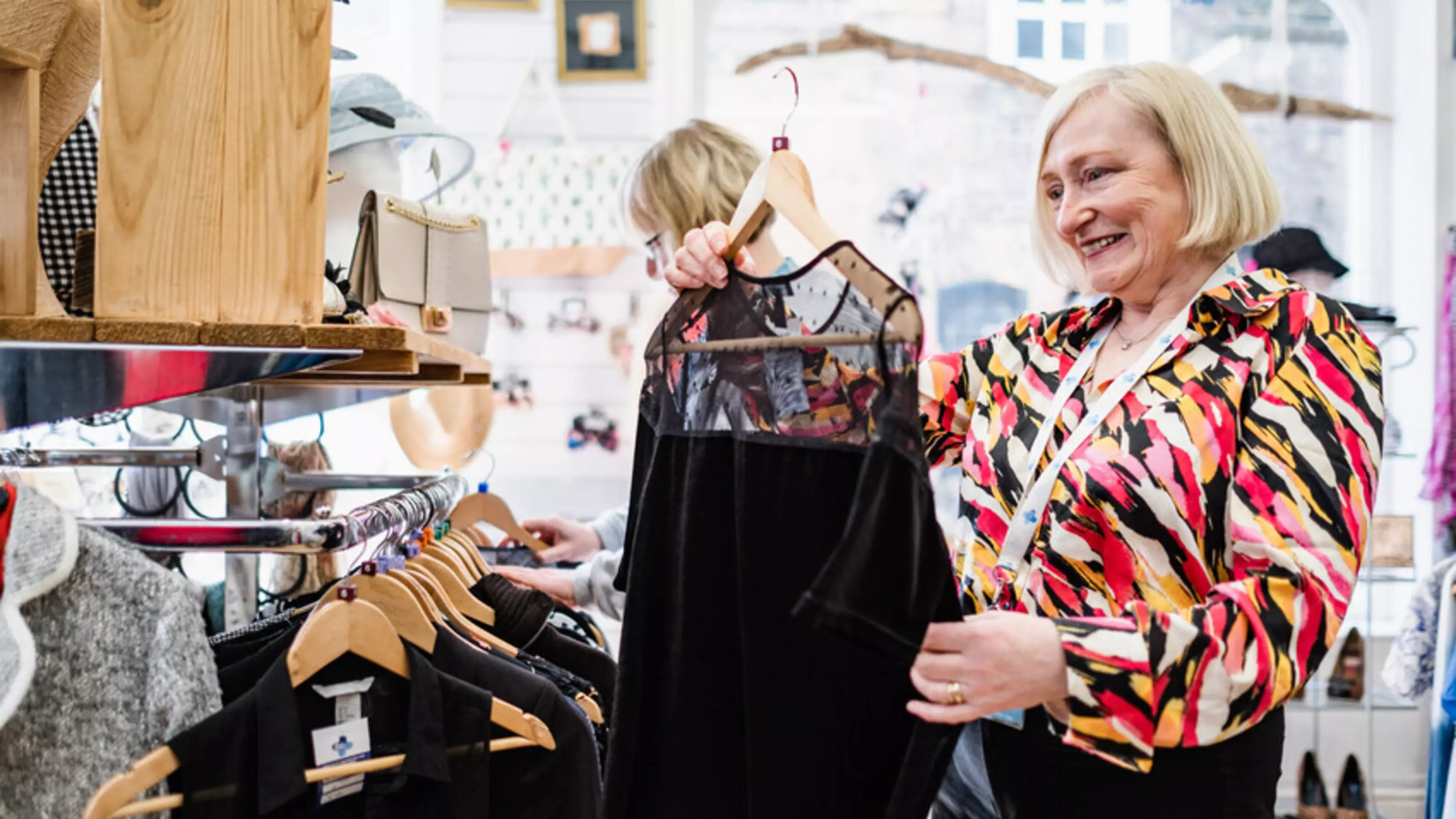 A female shop worker on the Blue Cross shop floor looking at a black dress on its hanger