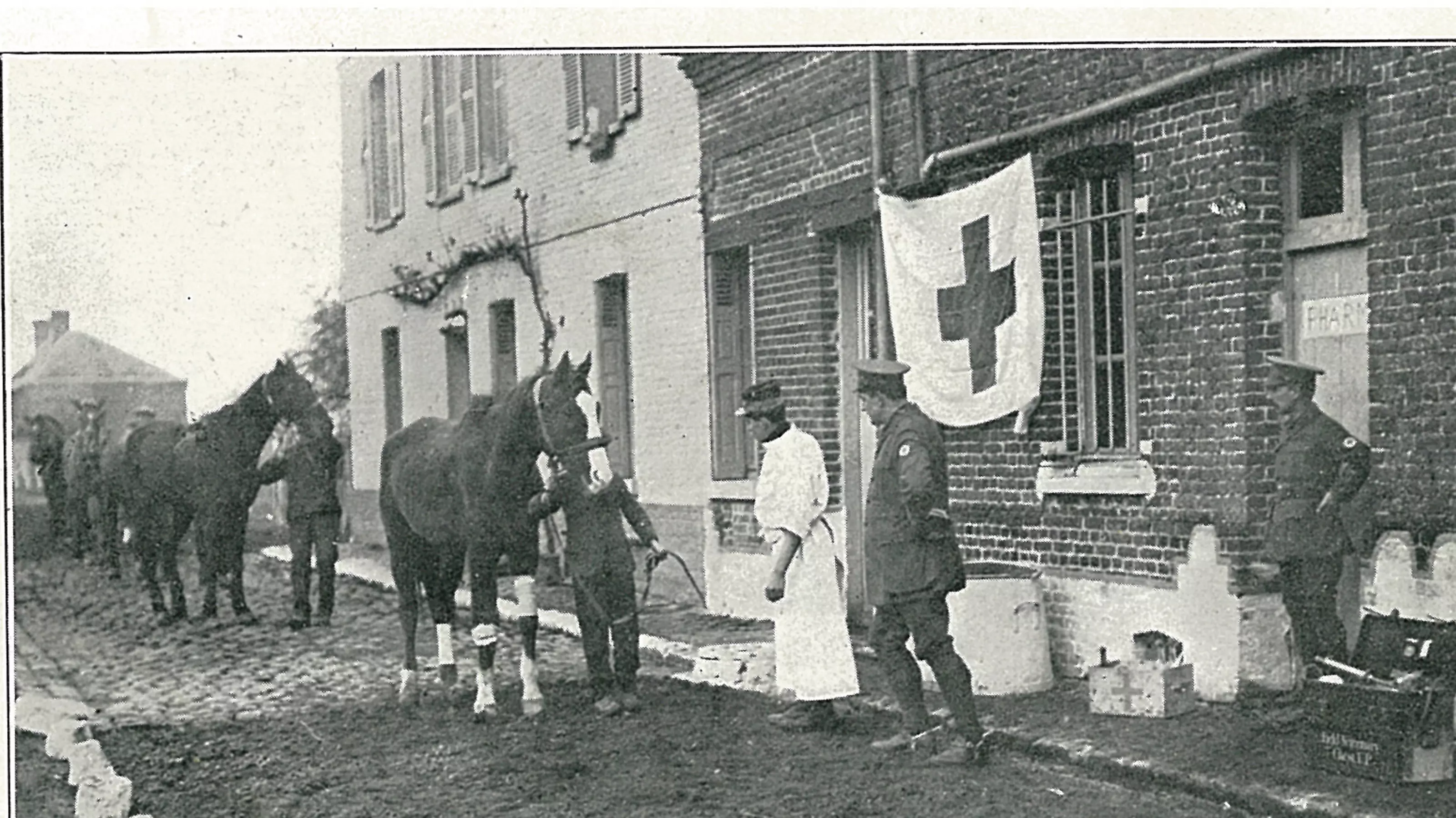 A blue cross flags hangs from a drainpipe outside a makeshift animal hospital in the First World War