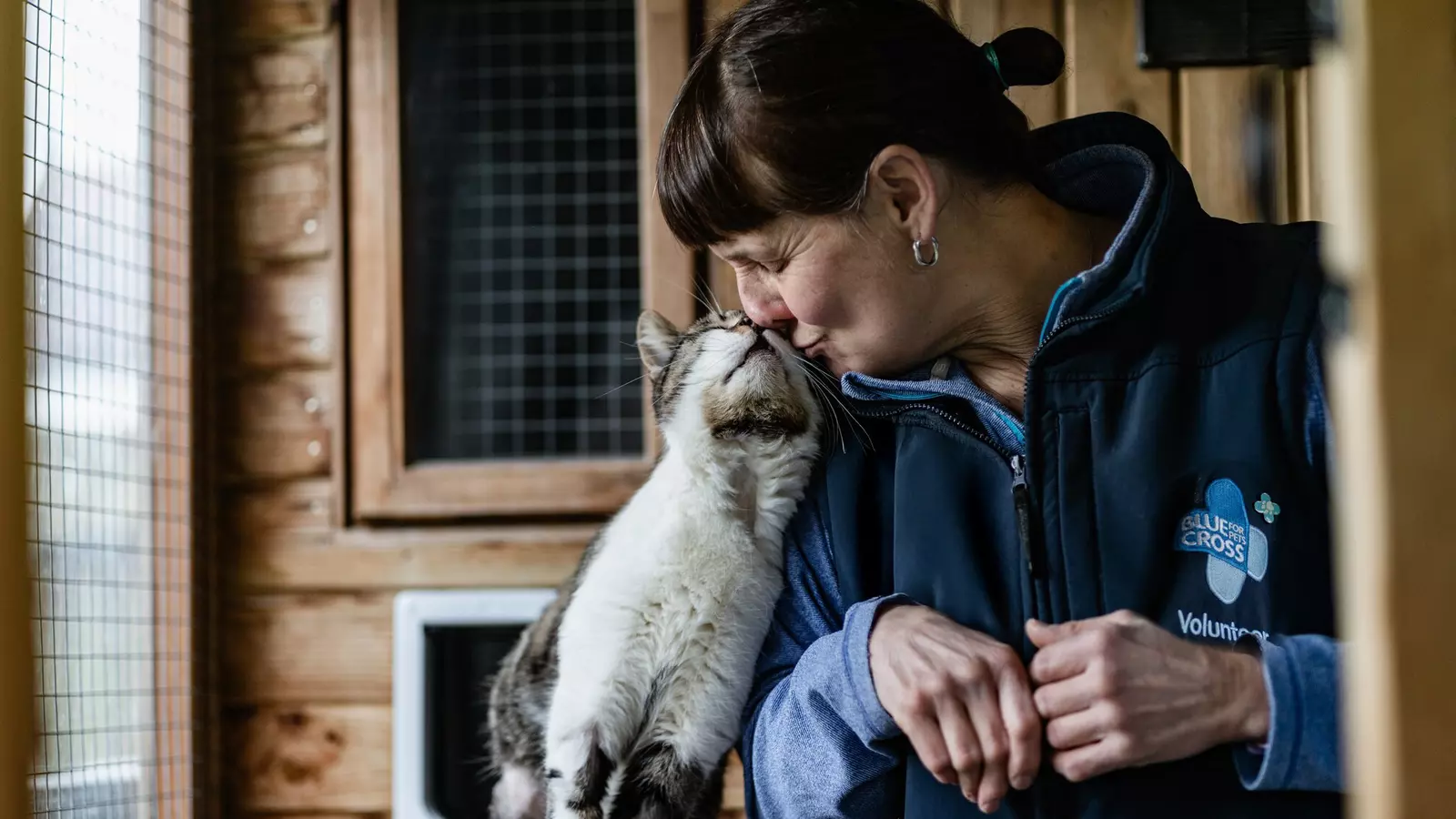 A Blue Cross volunteer is nuzzled by a tabby cat.