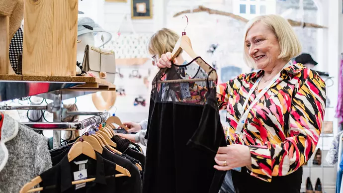 A female shop worker on the Blue Cross shop floor looking at a black dress on its hanger