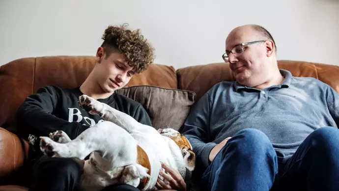 Dennis rolling on his back on the sofa with Ronnie fussing him