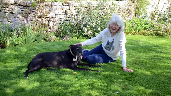 Bluebell and her owner Jilly Cooper sit down on grass in the shade