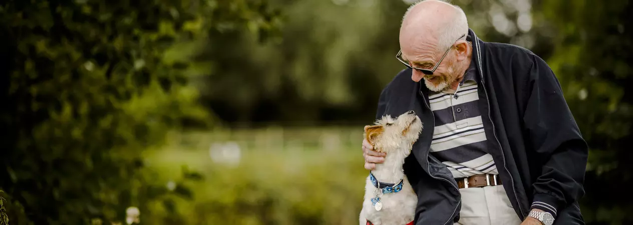 Photo of a jack russell terrier sitting next to a man. They are both looking at each other and smiling.