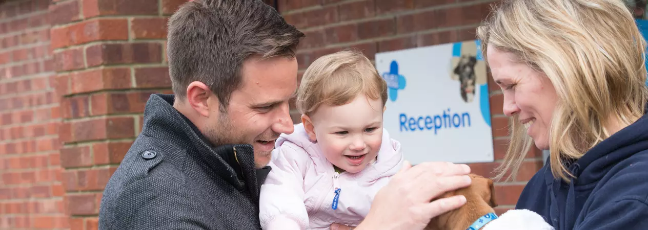 a man holds a young child to introduce her to a puppy. The puppy is being held by a Blue Cross member of staff.