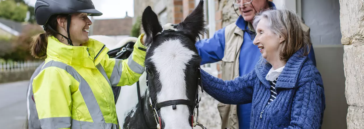 Black and white horse is stroked by woman and man outside their home