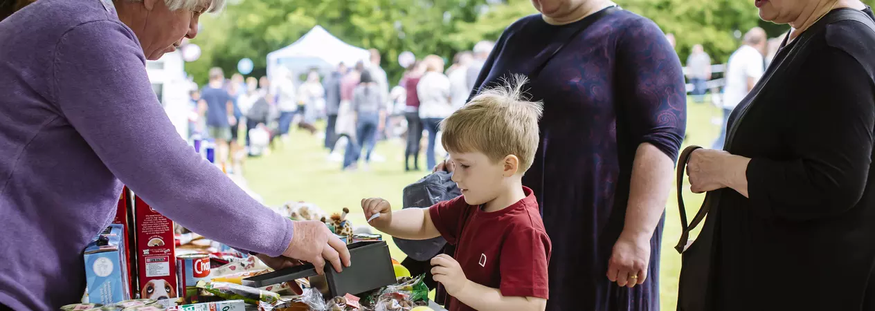 Young boy at fundraising stall putting money into the tin