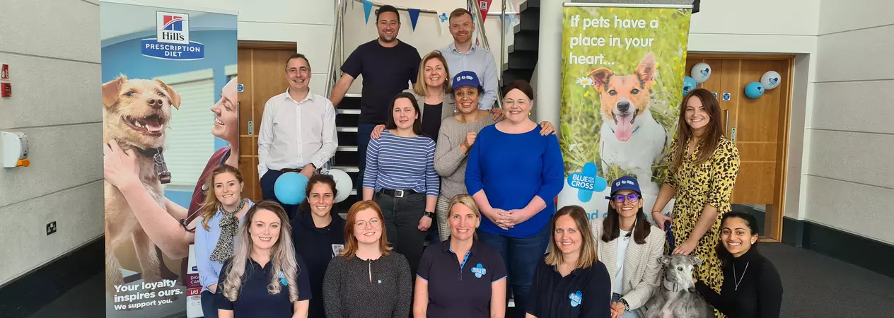 Blue Cross partner with Hills pet food. Blue Cross and Hills staff pose in front of Hills and Blue Cross banners.
