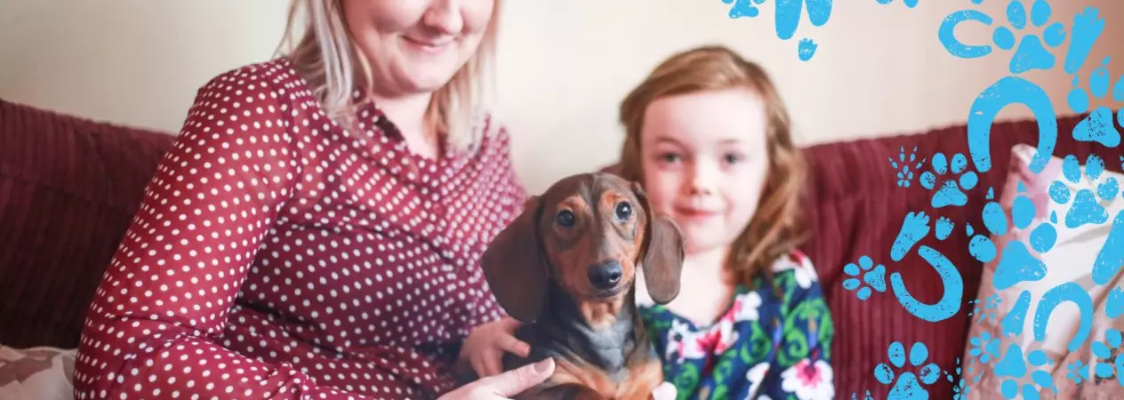 Woman and her daughter holding a small brown dog on their lap