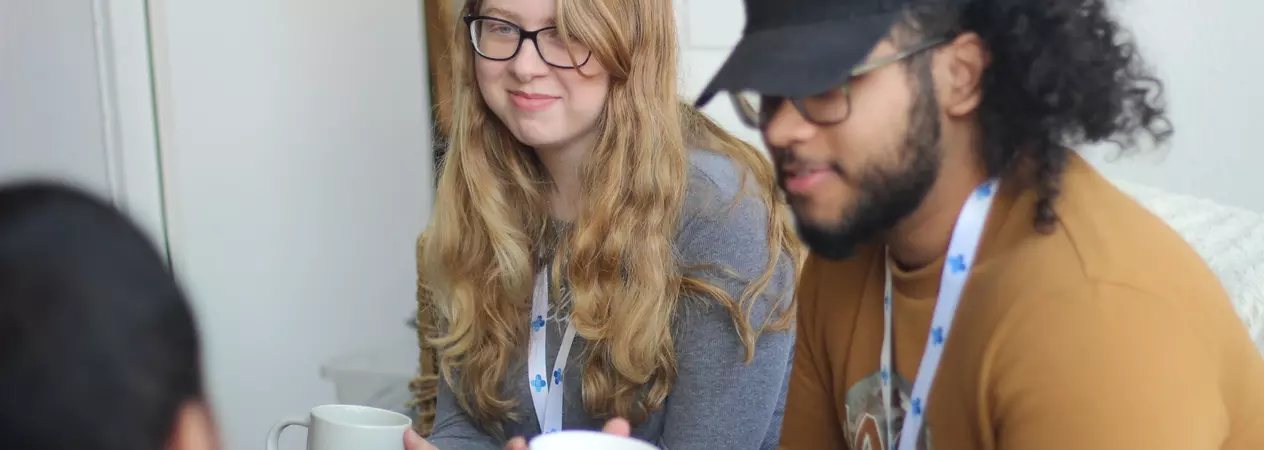 A young woman and young man sitting next to each other chatting over a cup of tea
