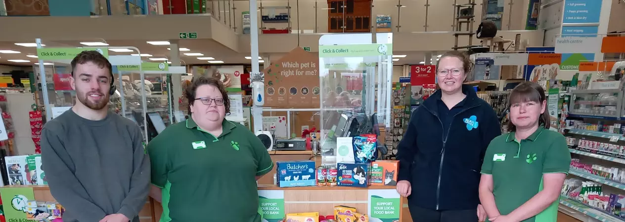 Four members of staff stand in a Pets at Home store with a pet food bank donation point at the till