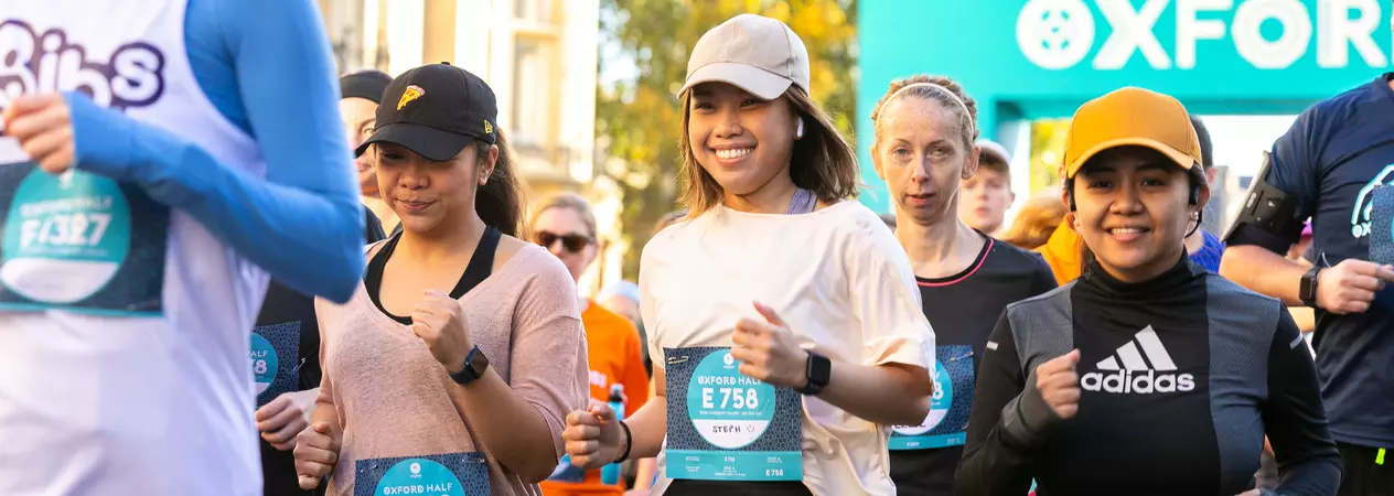 A group of runners taking part in the Oxford Half marathon. They are wearing caps and running gear, and smiling in the sunshine.