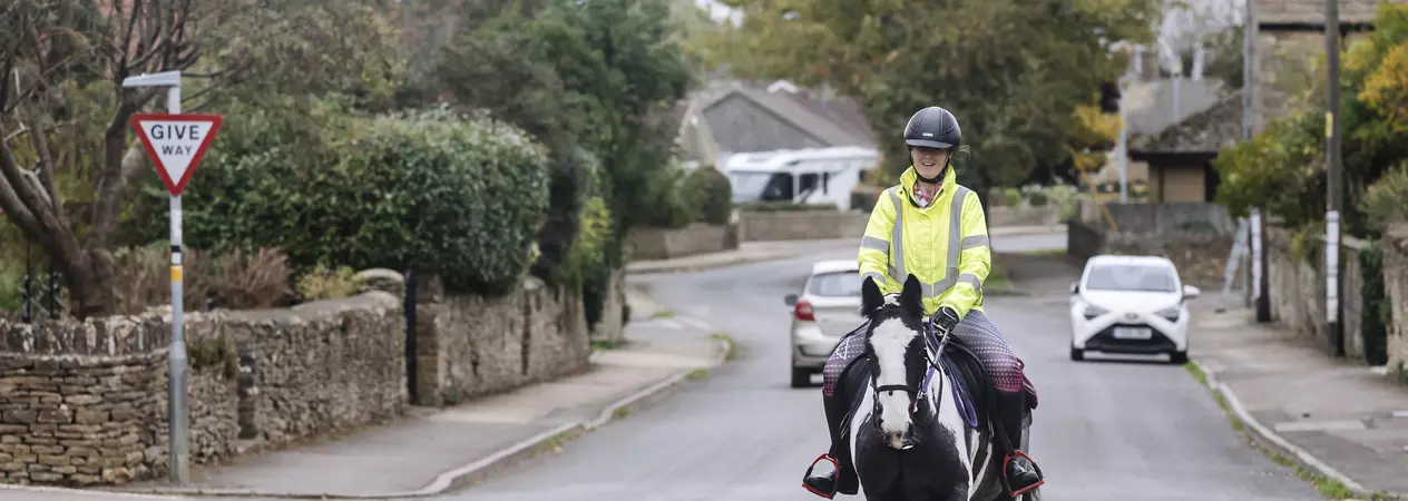 A horse and rider riding out on a road. The horse is black and white, and the rider is wearing a high visibility jacket.