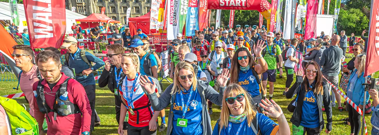 A group of participants of the North Yorks Ultra Challenge cross the starting line. They are waving at the camera and smiling.