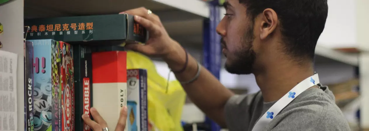 A young male volunteer sorting through boxed games in a Blue Cross charity shop