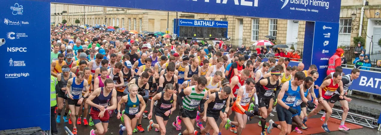 A crowd of people at the start line of a race with a big blue sign that says Bathalf 
