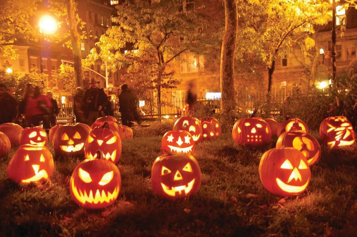 Multiple large carved pumpkins lit up in a small park 